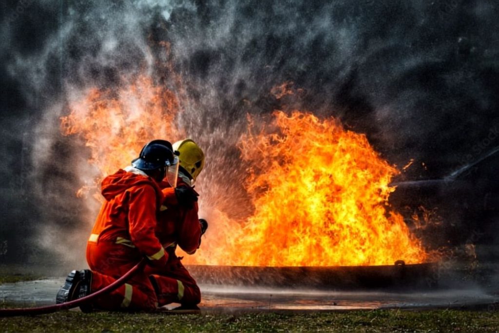 Two firefighters attacking a large fuel fire with a hose during fire suppression training